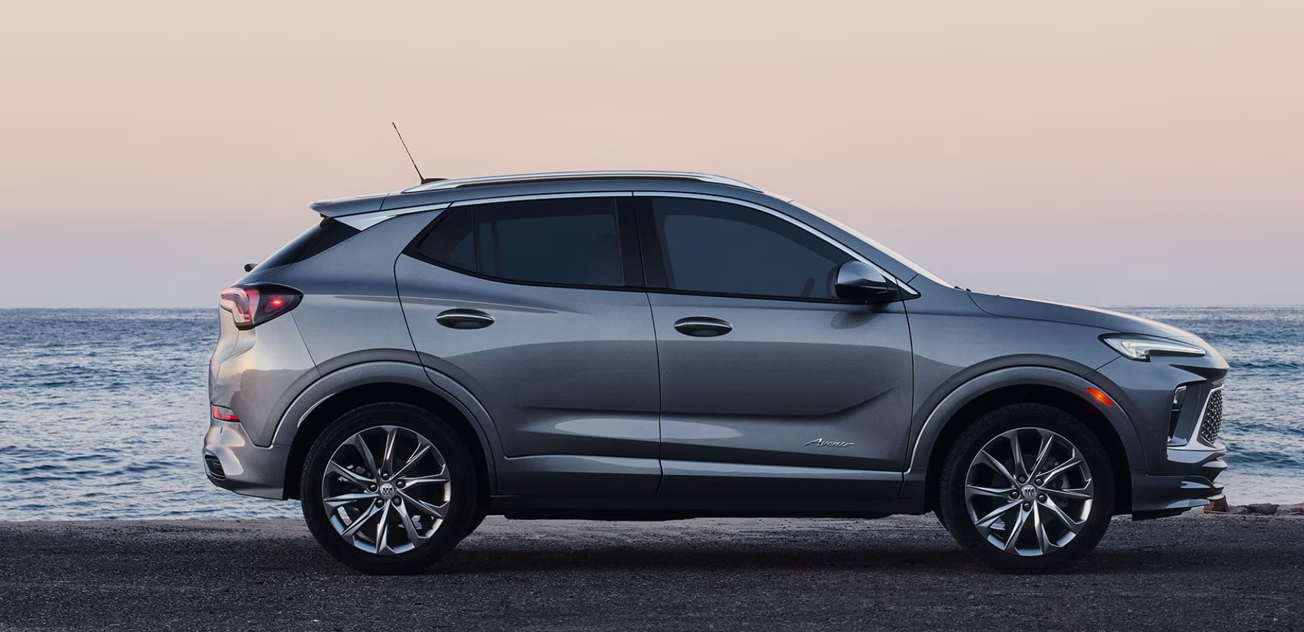 2026 Buick Encore GX Avenir in silver parked near the ocean at sunset.